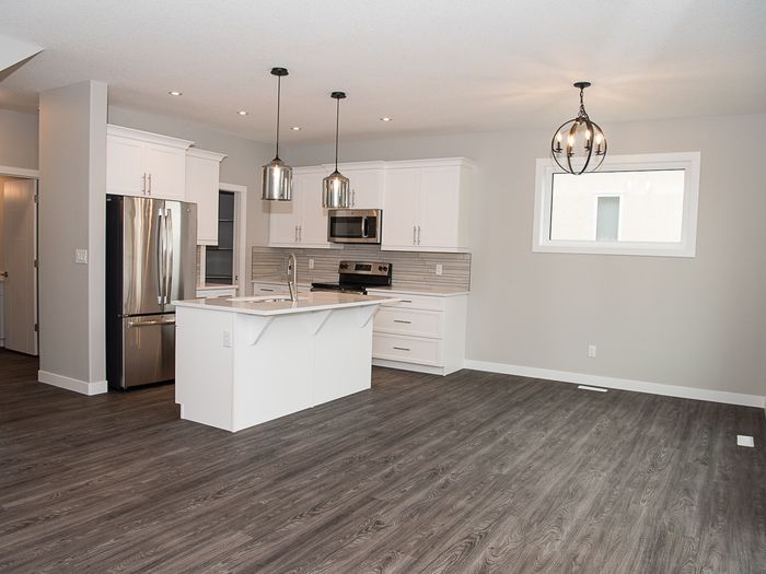 A kitchen floored in one continuous run under the island and appliances, with no transition strip at the doorways