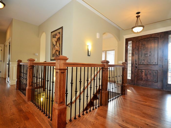 An upstairs landing with a wood railing, turned newel post and iron spindles, matched to the floor it opens onto